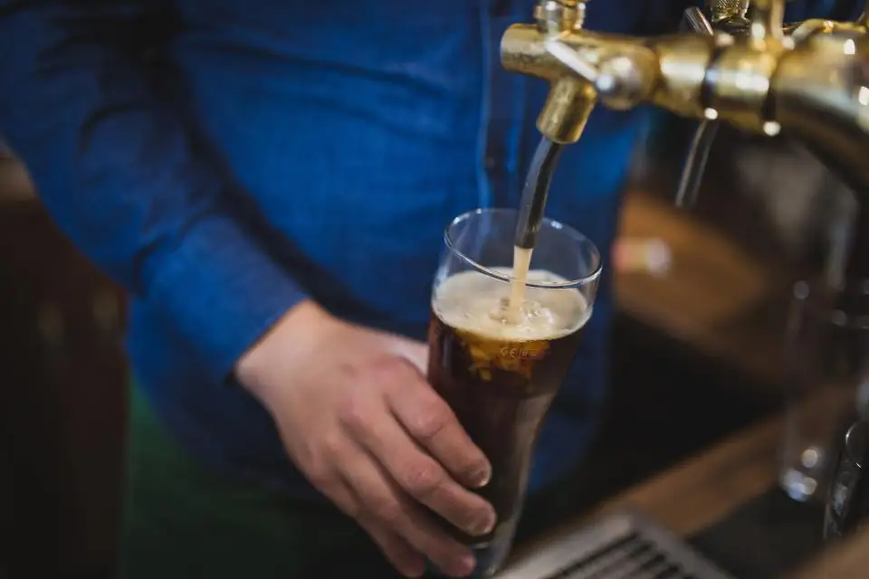 A bartender pulling a pint of dark beer from a brass tap